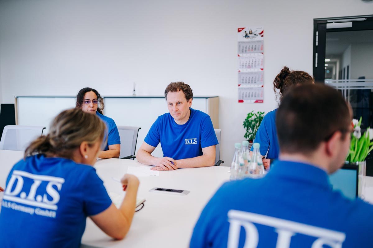 Vier Personen in blauen Hemden sitzen an einem Konferenztisch, fokussiert in einem Besprechungsraum.