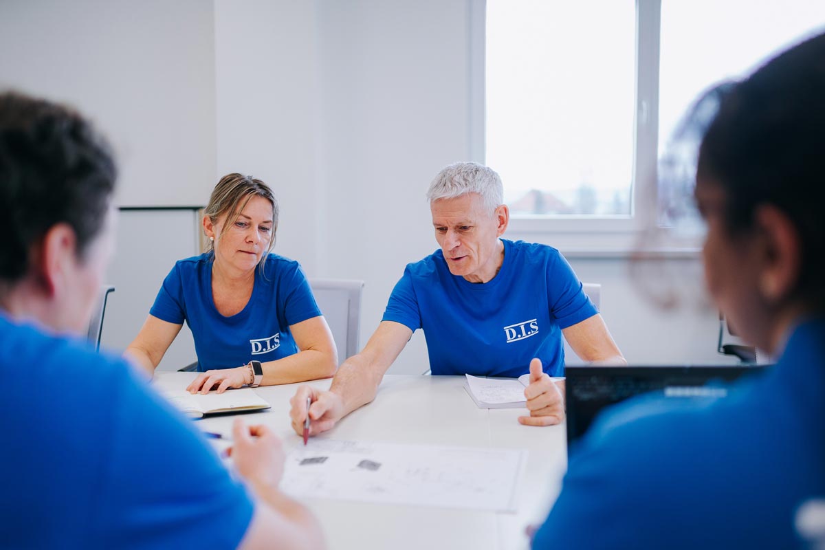 Mehrere Personen in blauen Hemden diskutieren ernsthaft an einem Tisch mit Papieren.