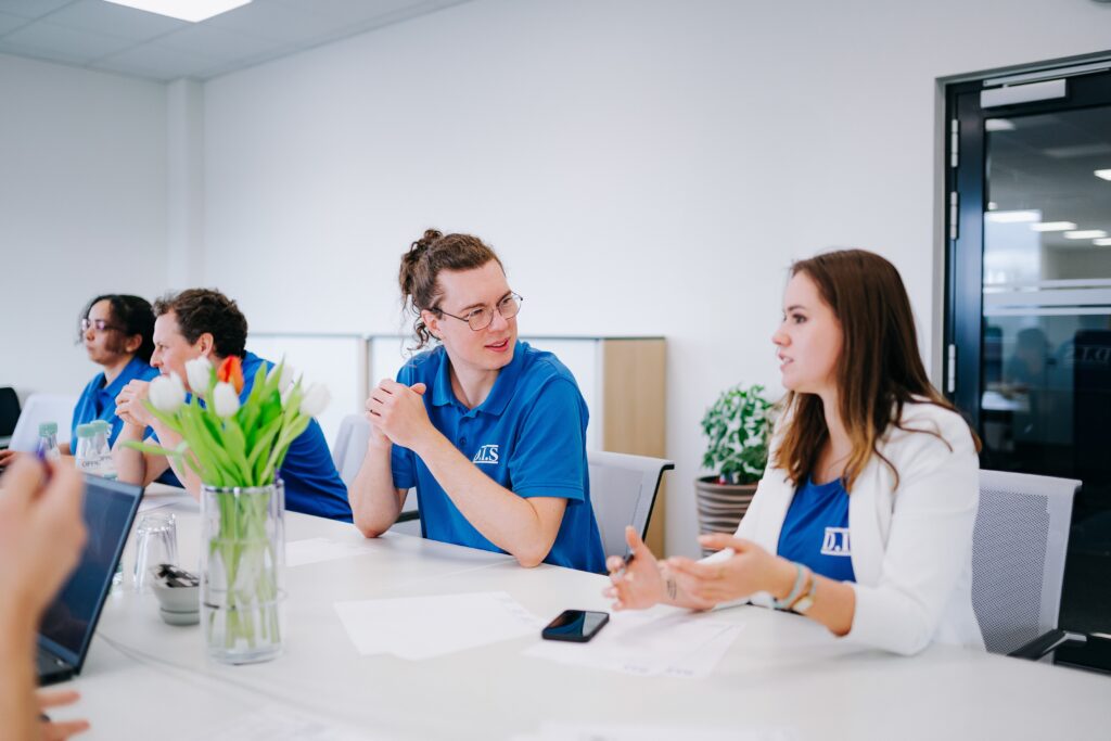 Eine Gruppe von jungen Menschen in blauen Hemden unterhält sich lebhaft in einem modernen Büro.