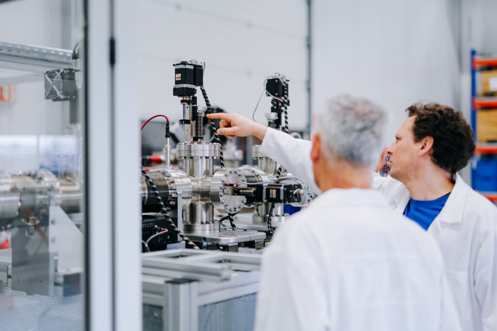 Zwei Wissenschaftler in Laborkitteln betrachten ein technisches Gerät in einem modernen Laborraum.