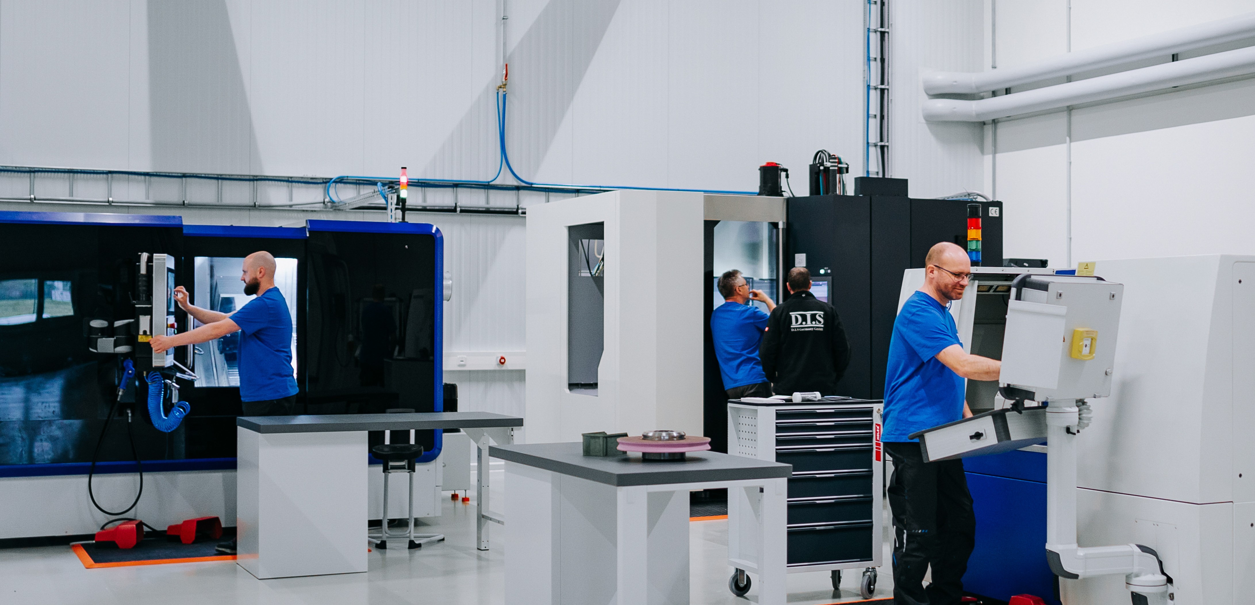 Drei Männer in blauen Hemden arbeiten in moderner Werkstatt mit Maschinen.