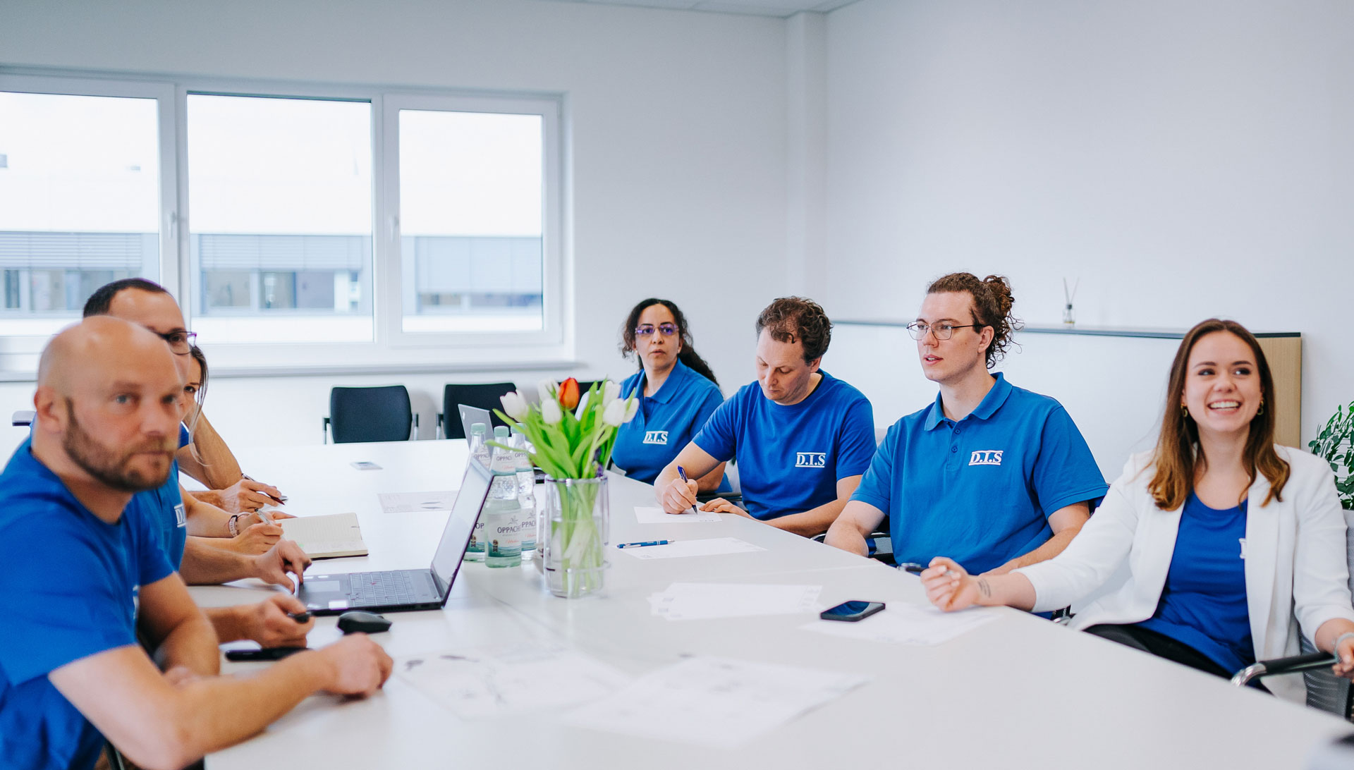 Mehrere Personen in blauen Hemden bei einem Meeting, entspannt lächelnd.