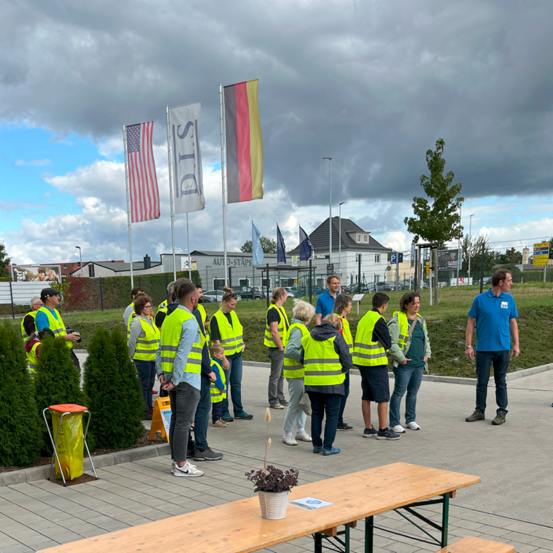Eine Gruppe von Menschen trägt gelbe Warnwesten und steht auf einem Parkplatz.