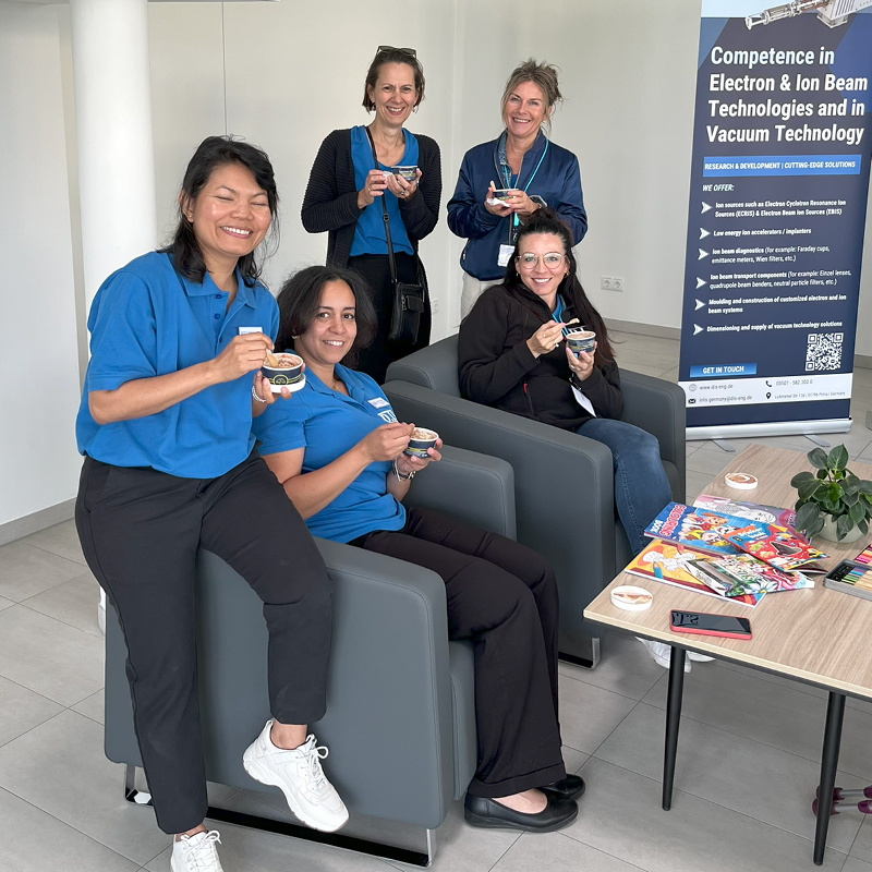 Eine Gruppe lächelnder Frauen in blauen Hemden sitzt auf grauen Sesseln.