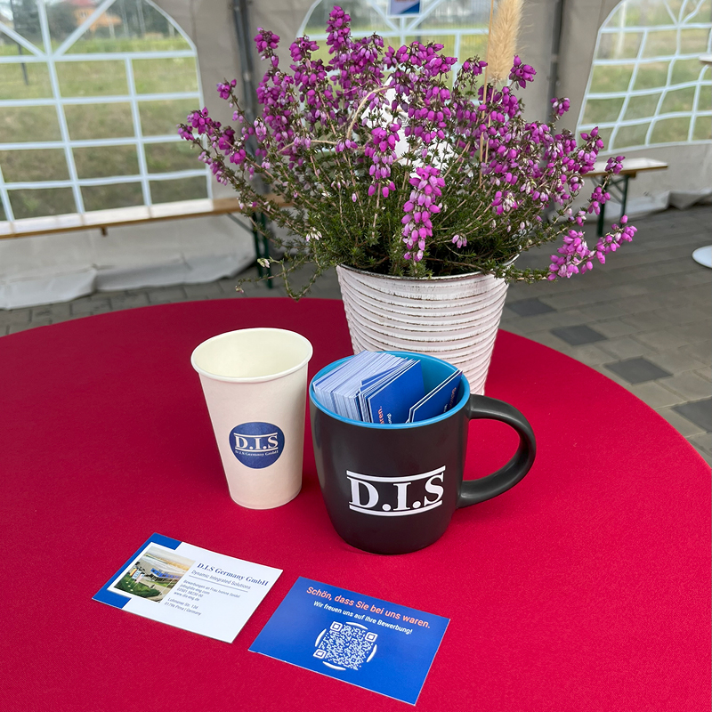 Ein roter Tisch mit einem lila Blumenstrauß und zwei D.I.S. Tassen.
