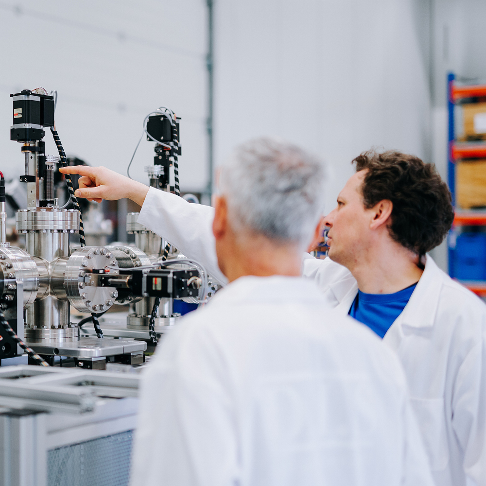 Zwei Männer in weißen Kitteln arbeiten konzentriert an technischer Ausrüstung.