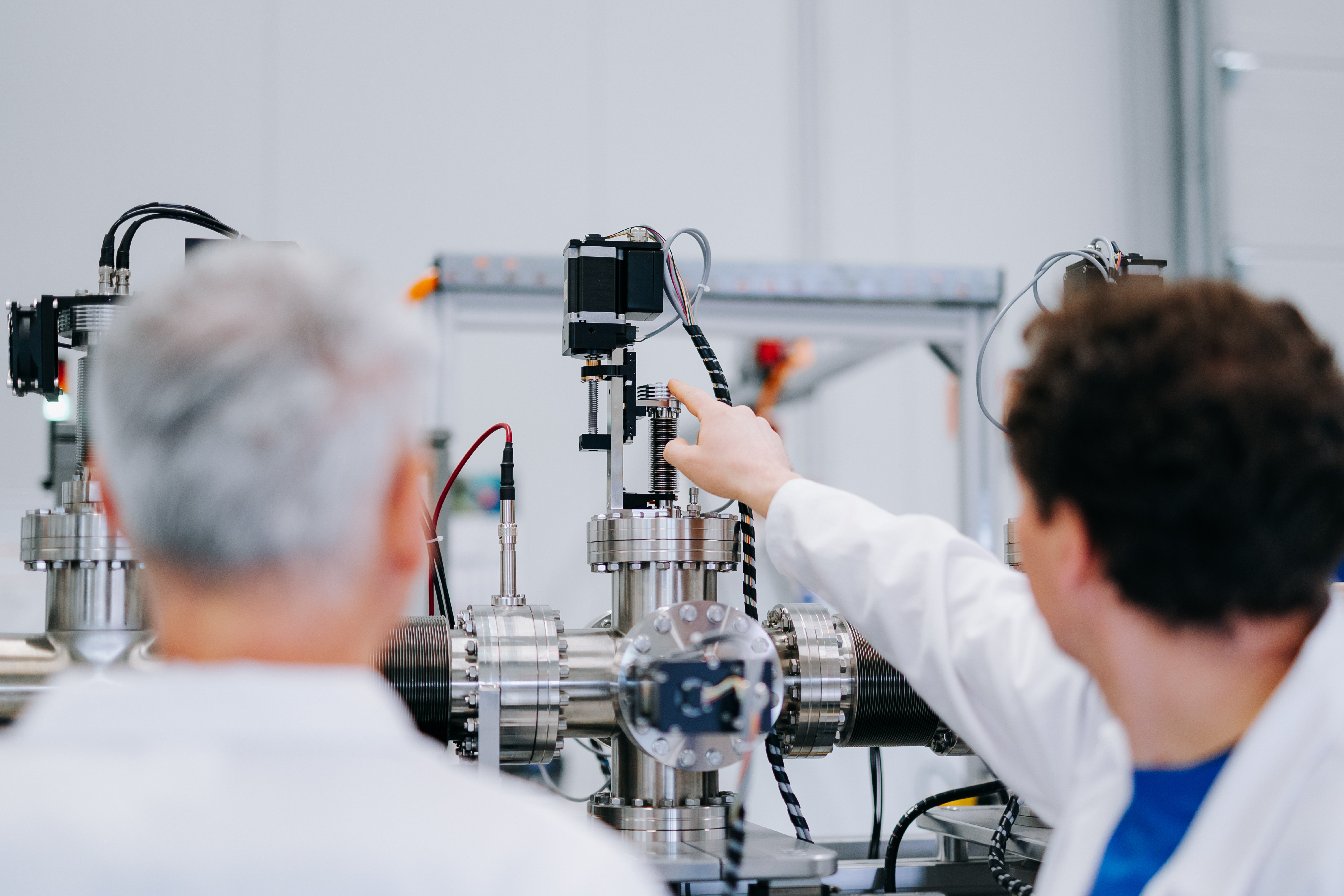 Zwei Männer in weißen Laborkitteln arbeiten an einer komplexen Maschine.