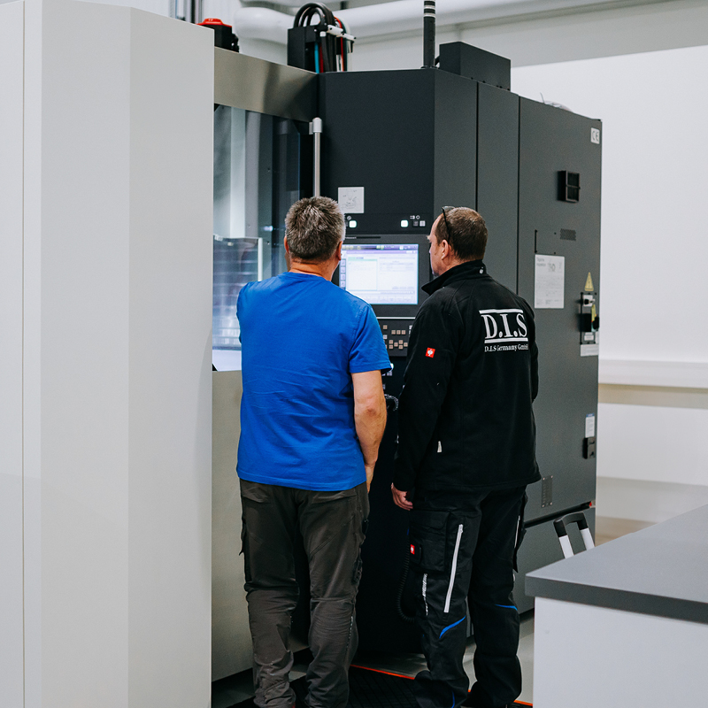 Zwei Männer schauen konzentriert auf einen großen schwarzen Automaten in einem hellen Raum